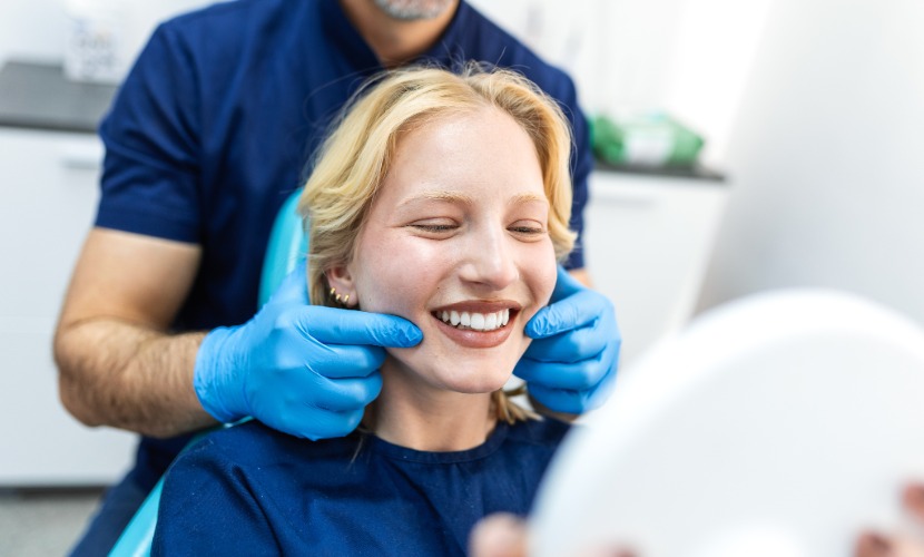 Paciente observa su sonrisa en un espejo mientras el dentista revisa sus dientes