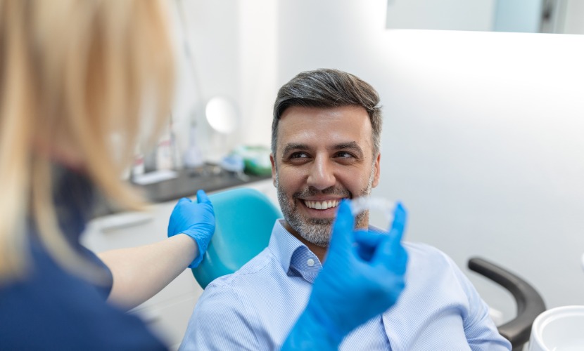 Paciente sonriente en el sillón dental mientras una profesional sostiene un alineador