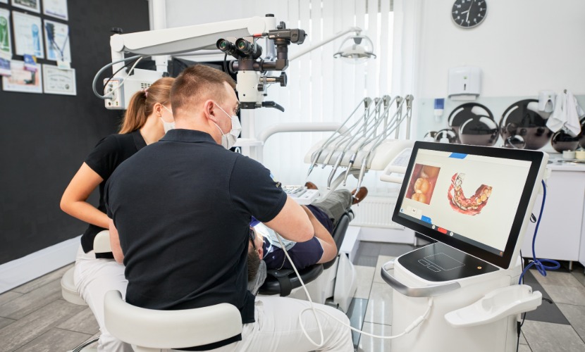 Profesionales atienden a un paciente junto a una pantalla con un modelo dental digital 3D